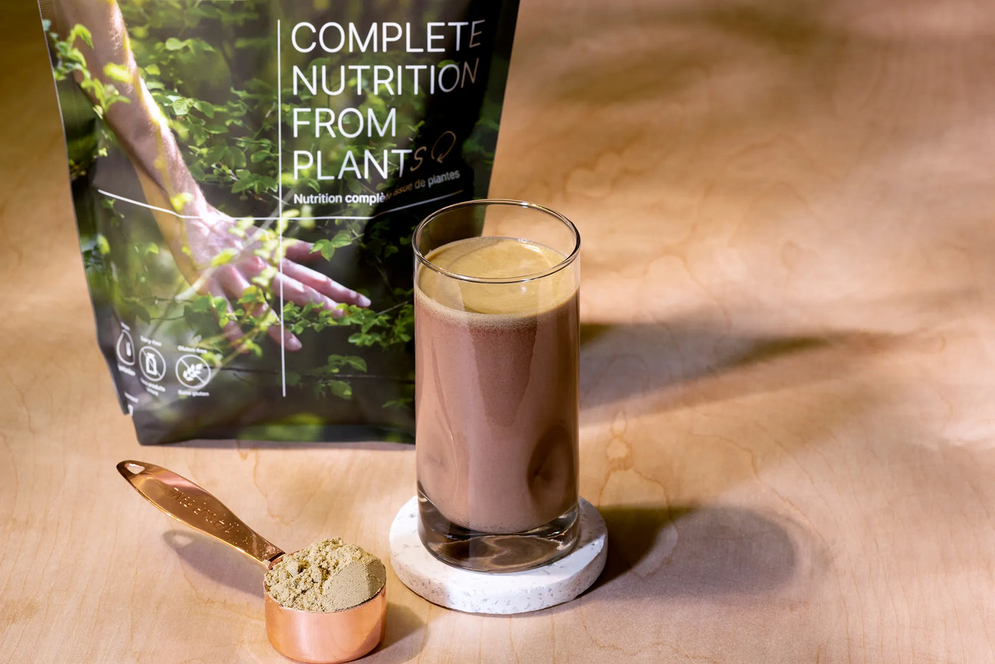 A glass of HEAL meal replacement, with the powder in a measuring spoon next to the glass, and the bag of HEAL in the background.