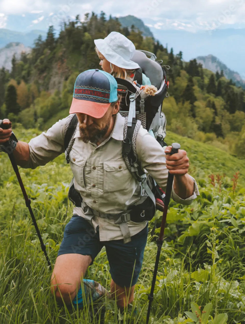 A man hiking in the mountains, with his daughter in a baby carrier backpack.