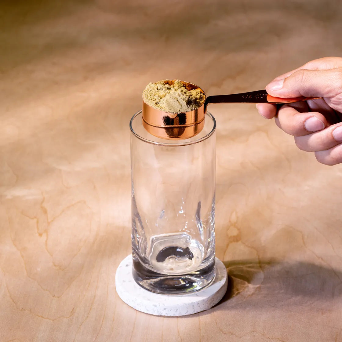 A hand holding a scoop of HEAL over an empty glass.